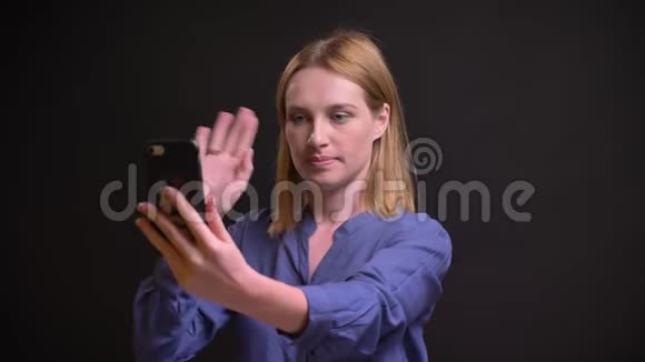 白种人金发女人穿着衬衫在黑色背景下使用智能手机在视频聊天的肖像视频的预览图