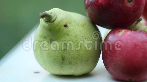 成熟的水果绿梨红苹果和黄樱桃李躺在一张白色的乡村桌子上背景是绿色的花园视频的预览图