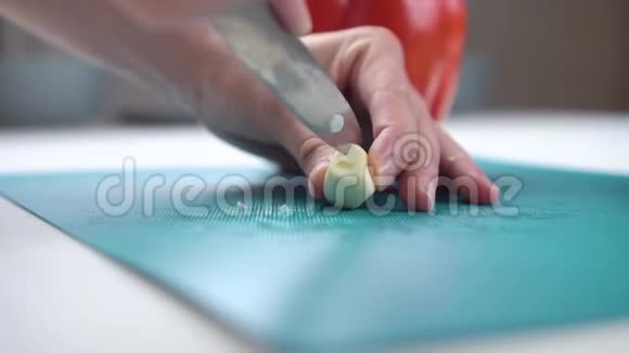 女性的手在背景上用红胡椒在切割板上切割大蒜视频的预览图