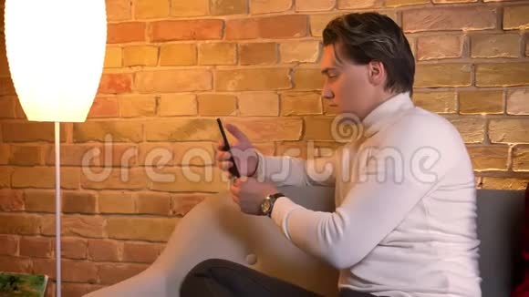 多莉拍摄的年轻白种人夫妇背靠背坐在沙发上智能手机在家里的气氛视频的预览图