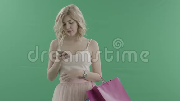 漂亮的年轻女性在购物后等待某人并在智能手机上用绿色屏幕发短信视频的预览图