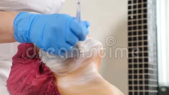在美容院戴面膜的漂亮女客户在女性脸上涂面膜用刷子视频的预览图