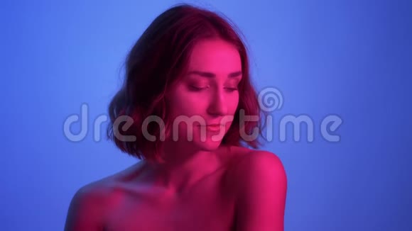 年轻性感女性的特写镜头裸露的肩膀看着镜头带着霓虹的蓝色和诱人的微笑视频的预览图