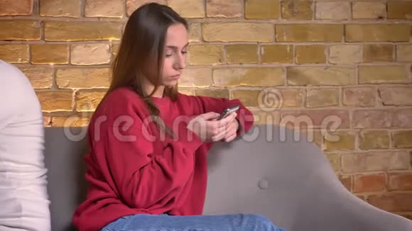 多莉拍摄的年轻白种人男女背靠背坐在沙发上智能手机在家里的气氛视频的预览图