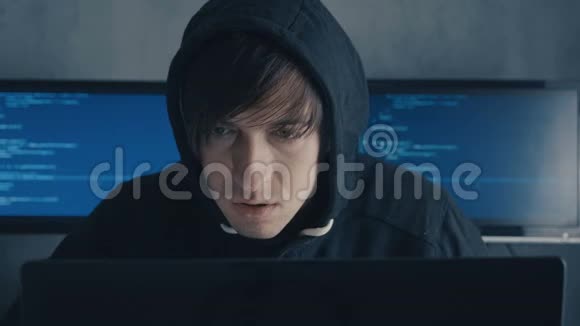 戴帽子的人坐在桌子上在笔记本电脑上编码戴帽子的家伙在数据中心的计算机上工作充满了监控视频的预览图