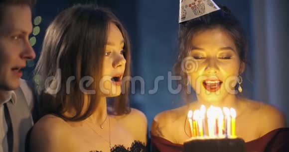 漂亮的微笑女孩在一个聚会上在朋友围着的生日蛋糕上吹蜡烛一个女孩和一个视频的预览图