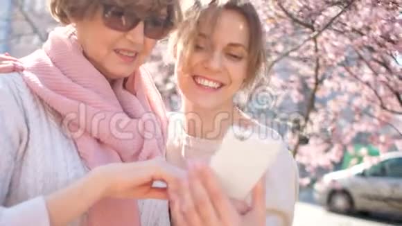 一个成熟的女人和她的年轻朋友带着智能手机的快乐肖像女性友谊女性商业网络视频的预览图