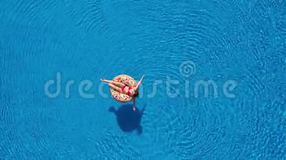一位穿红色比基尼的女士躺在游泳池的甜甜圈上的空中景色视频的预览图