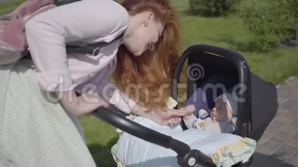 美丽的红发女人俯在公园里的一辆电车上这位女士和她的孩子在户外享受阳光明媚的一天青年视频的预览图