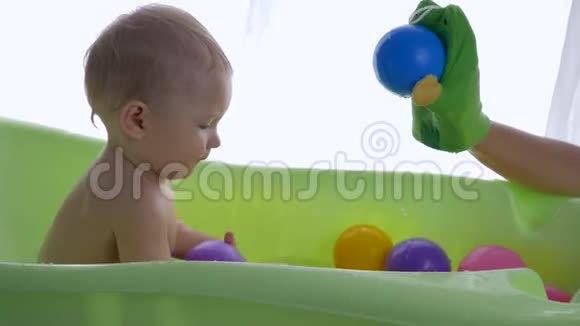 快乐的童年父母手玩具玩可爱的幼儿男孩洗澡与彩色球在明亮的房间视频的预览图