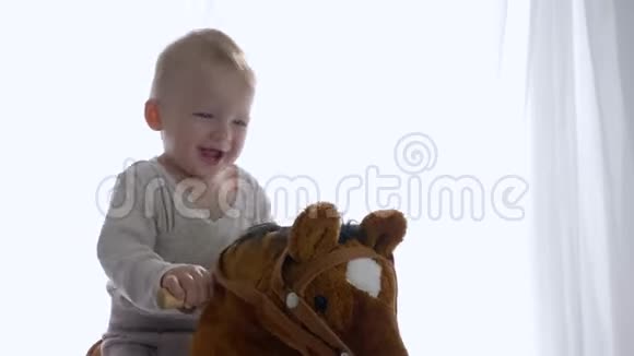 孩子的情绪快乐欢快的小男孩喜欢在房间里骑玩具马视频的预览图