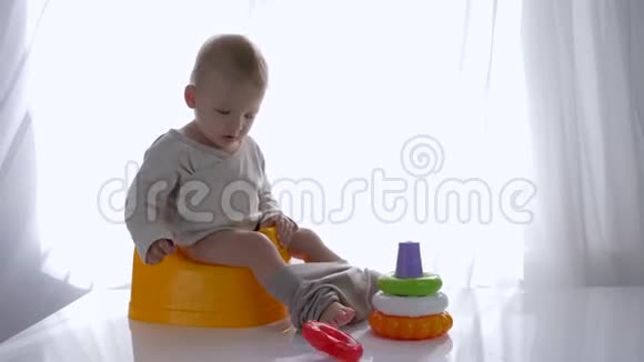 在明亮的房间里培养宝宝坐在室内锅上玩彩色玩具金字塔视频的预览图