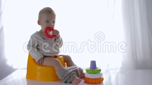 可爱的幼儿坐在马桶上在明亮的房间里玩教育塑料玩具金字塔视频的预览图