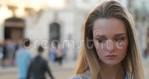 一个美丽的金发女孩在街上闲逛的肖像然后用她明亮的大眼睛对着镜头上光视频的预览图