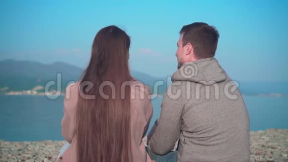 春天一个留着长发的年轻女孩和一个男人坐在海滩上那个女孩和那个相框里的家伙旋转视频的预览图