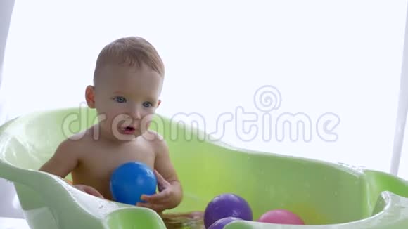 快乐纯洁的小男孩希望在明亮的房间里洗澡后用彩色球洗澡视频的预览图