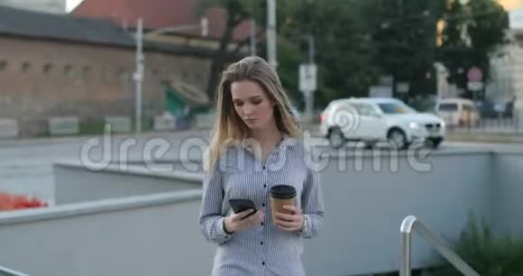 一位迷人的年轻女士正在街上散步她打字时手里拿着咖啡和电话视频的预览图