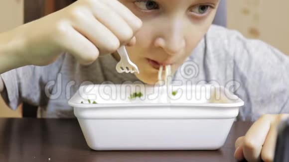 一个十几岁的白种人男孩在家吃中国快餐从一次性容器里的方便面视频的预览图