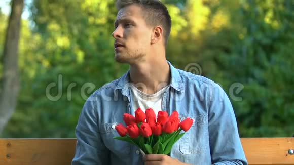 紧张的男人一堆郁金香坐在长凳上等女朋友约会视频的预览图