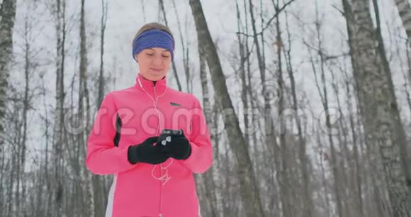 一位正在晨间慢跑的年轻女子手里拿着一部智能手机挑选一首音乐曲目进行训练冬季跑步使用视频的预览图