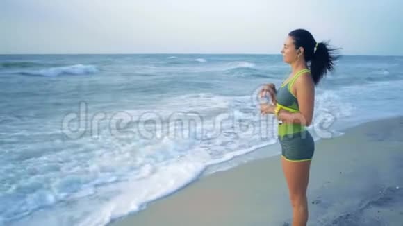 戴着耳机的女人在海上慢跑中间休息时体贴地喝水视频的预览图