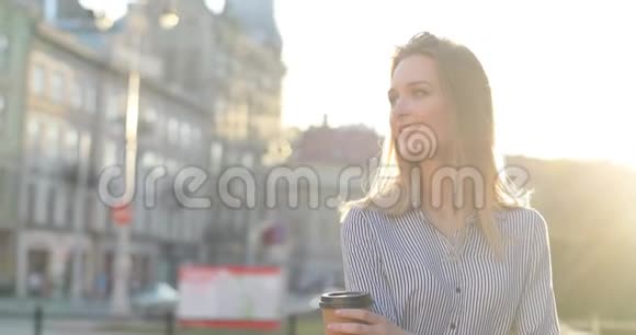 一位美丽的年轻女士正在大街上喝着她的早间咖啡对着镜头微笑特写肖像视频的预览图