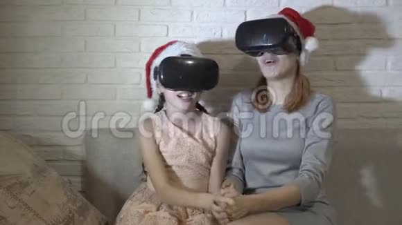 快乐的孩子们戴着虚拟现实头盔头上戴着圣诞老人的帽子坐在家里的沙发上对着一个视频的预览图
