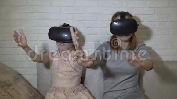 两个穿着黑色虚拟现实眼镜的年轻女孩坐着玩虚拟游戏他们挥动双手按虚拟视频的预览图