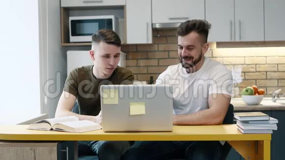 两个人在一台电脑上学习和工作用一本教科书坐在家里的厨房里彼此交谈视频的预览图