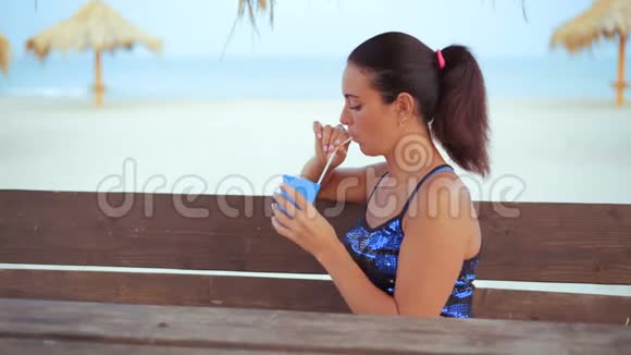 坐在海边的木桌旁的一个漂亮的浅棕色女人的鸡尾酒视频的预览图