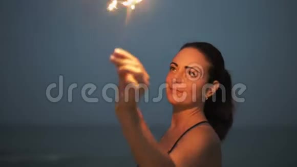 在海边美丽的昙花一现的女人在深夜挥舞着燃烧的孟加拉火视频的预览图