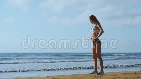 女孩穿着运动服腿站在海洋附近缓慢地抚摸着她的头发视频的预览图