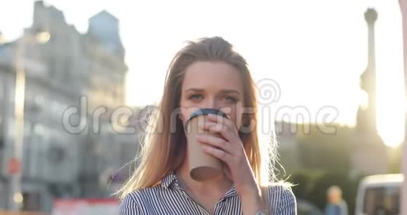 一个漂亮的女孩正在市中心喝着早晨的咖啡微笑着太阳正照在相机视频的预览图