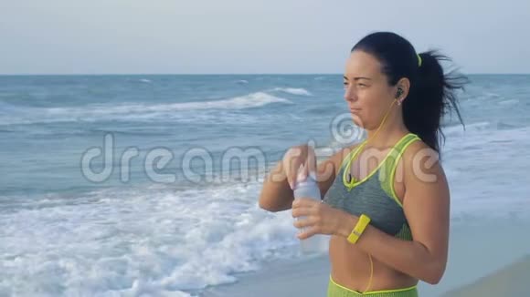 慢动作美丽的女人站在海边早上慢跑后喝水视频的预览图