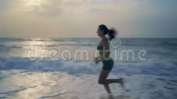 黎明时分美丽的女人在海滨的耳机里参与体育运动视频的预览图