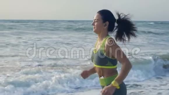 慢动作耳机里的美丽女人在海边奔跑引领健康的生活方式视频的预览图
