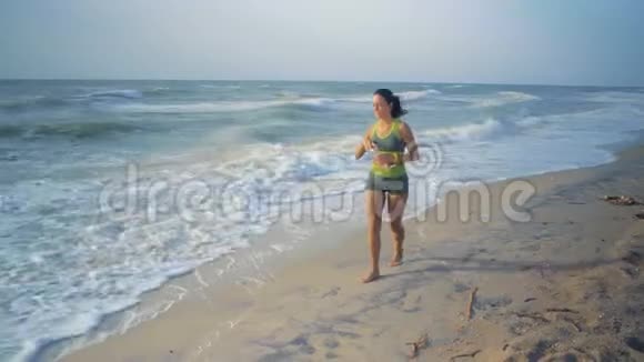 美丽的女人在耳机停留在海岸和喝水后晨跑视频的预览图