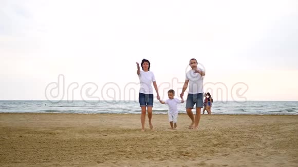 一个幸福的三口之家走在沙滩上望着天空用一只手缓慢地显示出来视频的预览图