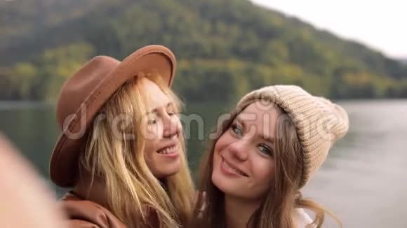 两个迷人的女孩年轻女性时尚地穿着度假的衣服在山上的湖上拍摄视频聊天自拍视频的预览图