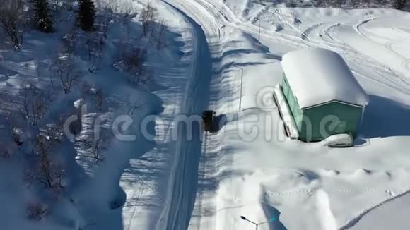 一辆黑色的汽车正行驶在城外的积雪覆盖的道路上空中拍摄的画面是4k视频的预览图