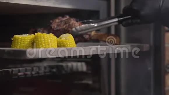 用黑色手套的厨师手用钳子把烤炉里的带肋肉取出切片的玉米在视频的预览图