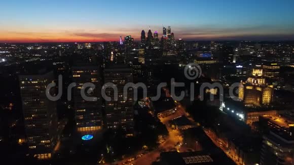 令人印象深刻的4k空中无人驾驶飞机飞越温暖的橙色傍晚日落天空在城市明亮的夜光照明城市景观视频的预览图