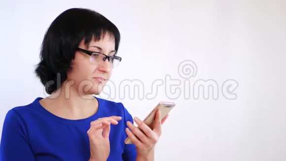 带眼镜的布鲁内特女孩在白色背景下使用智能手机女孩用手指触摸智能手机视频的预览图
