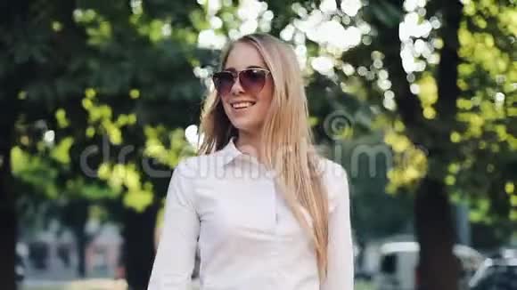 美丽的年轻商务女性带着太阳镜步行穿过城市看着城市的郊区视频的预览图