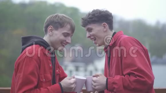 两个穿红色夹克衫的年轻人喝着咖啡杯微笑着在户外玩耍视频的预览图