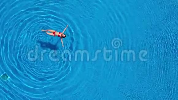 从顶部看一个穿着红色泳衣的女人躺在游泳池的背上放松概念视频的预览图