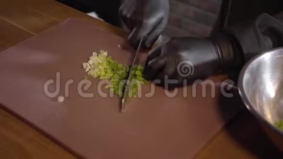 一个穿着黑色橡胶厨师手套的厨师在切割板上切下新鲜洋葱然后把它扔进铁碗里视频的预览图