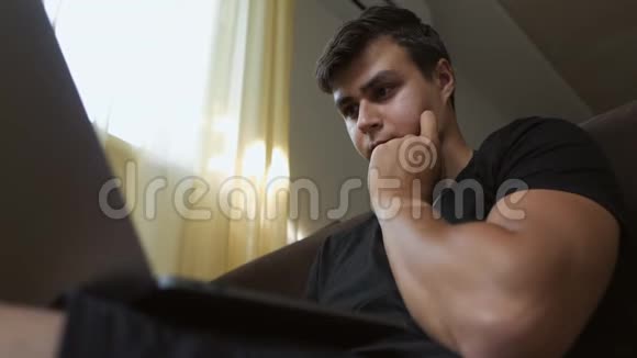 一个年轻人坐在窗边的房间里用笔记本电脑一个表情严肃的自由职业者视频的预览图