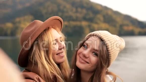 两个迷人的女孩年轻女性时尚地穿着度假的衣服在山上的湖上拍摄视频聊天自拍视频的预览图