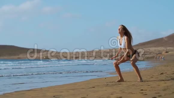 穿着运动服装短裤和t恤的女孩在加那利群岛海边的海滩上蹲着跳视频的预览图